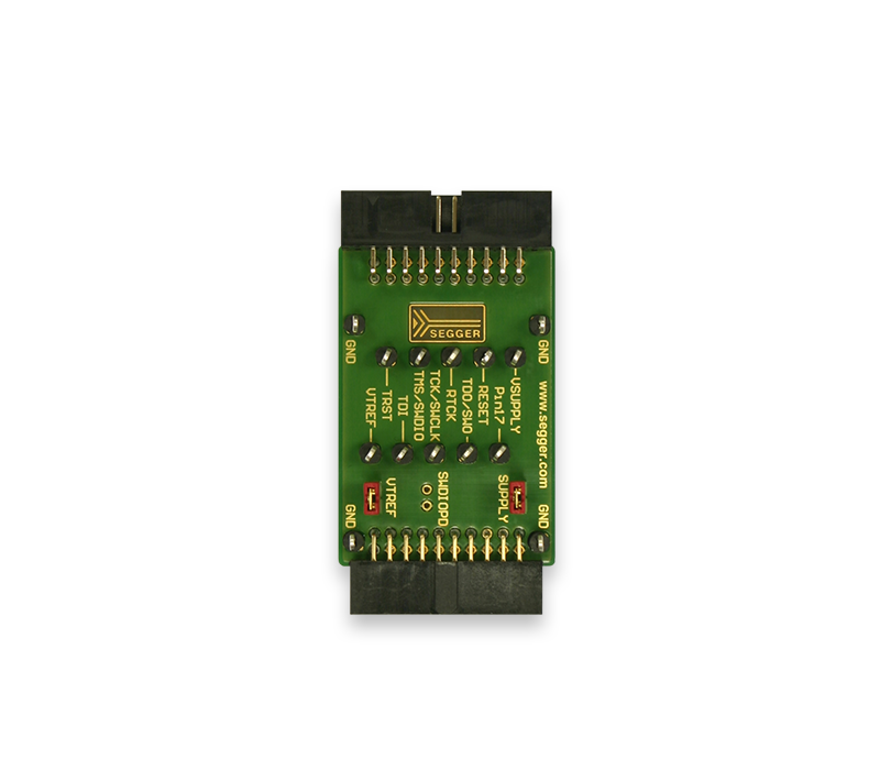 A green electronic circuit board with multiple pin connectors is displayed. The board features labels such as "GND," "U-SUPPLY," and "I/O." The SEgger logo is visible at the center, indicating it is a device component, possibly for programming or debugging electronics.